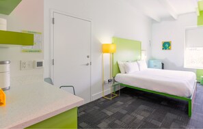 Ein Hotelzimmer mit einem Bett, einem Schreibtisch, einer Lampe, einem kleinen Schrank und einer Tür.