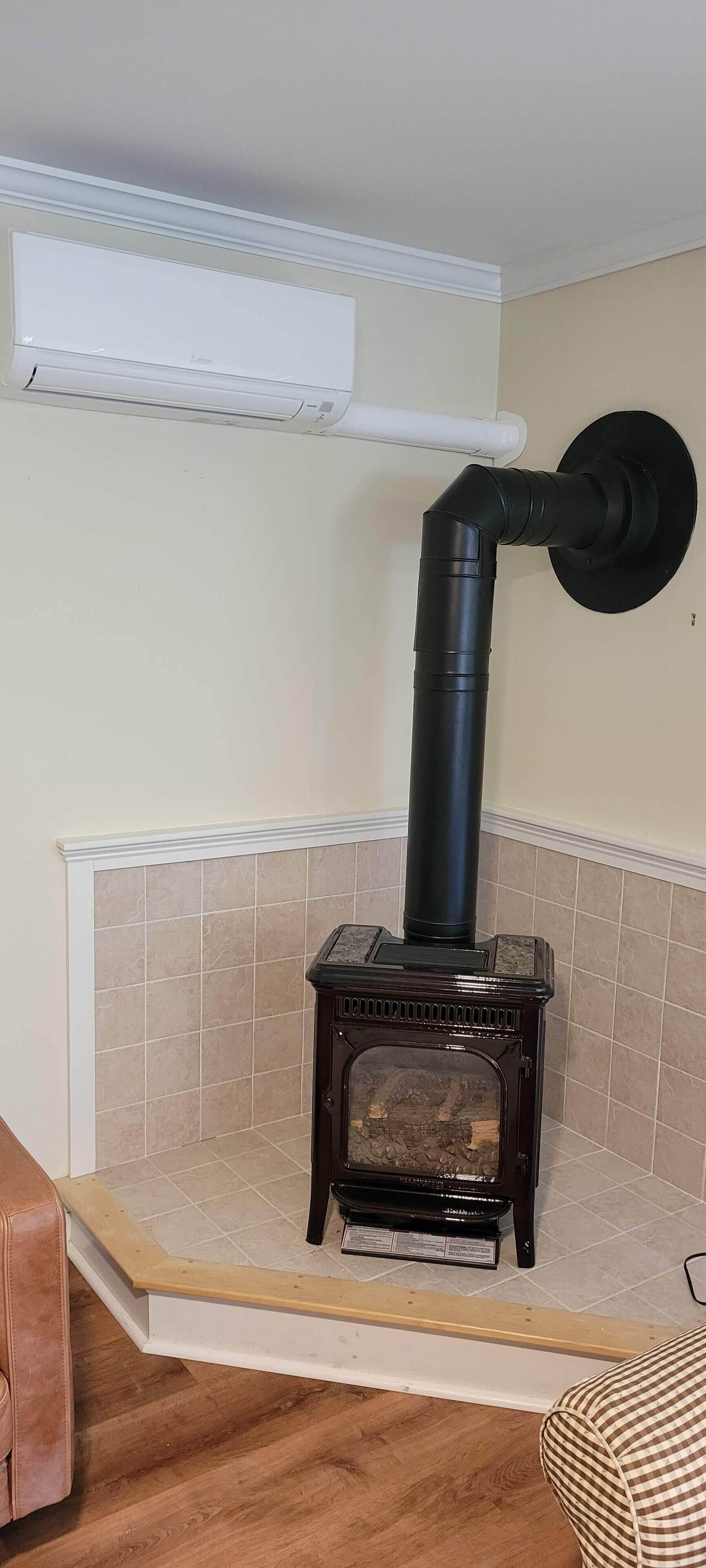 A wood-burning stove with a black chimney, a white vent, and a tiled floor.