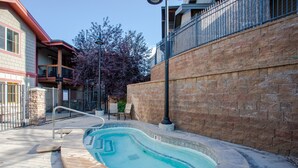Una piscina con borde de piedra, barandilla metálica y pared de ladrillo cerca.