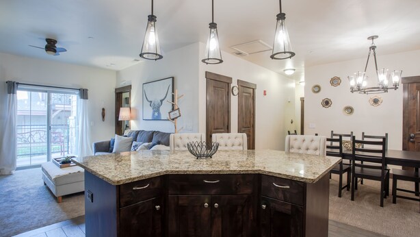 Una cocina con isla de granito, armarios de madera oscura, luces colgantes y una zona de comedor con sillas y mesa de madera.