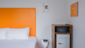 A hotel room with a bed, a white toilet, a small wooden cabinet with a safe, and a wall clock. - The Gallatin (320) Colorful Boutique Hotel! (Nashville)