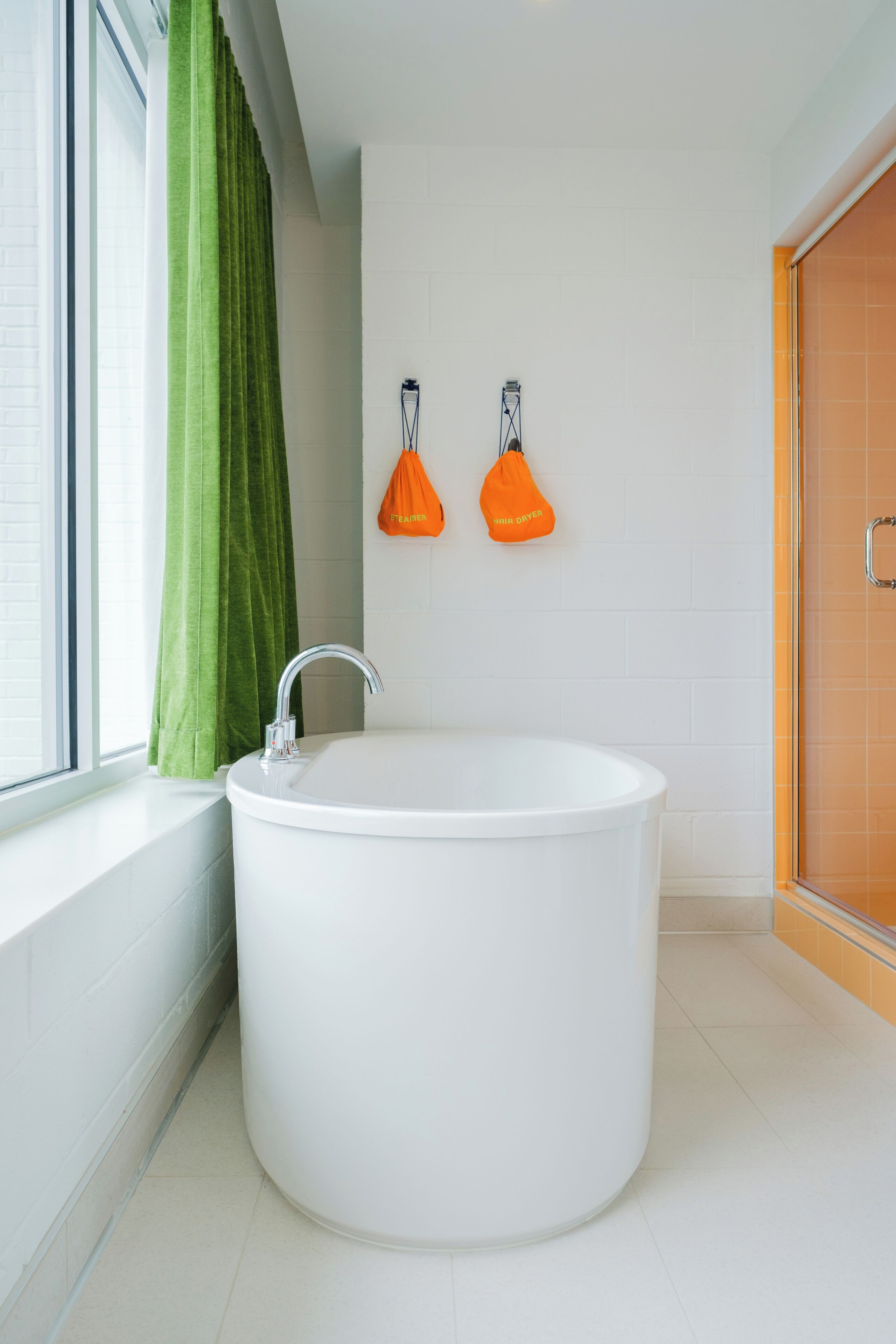 A modern bathroom with a freestanding bathtub, a window with curtains, and two wall-mounted hair dryers.