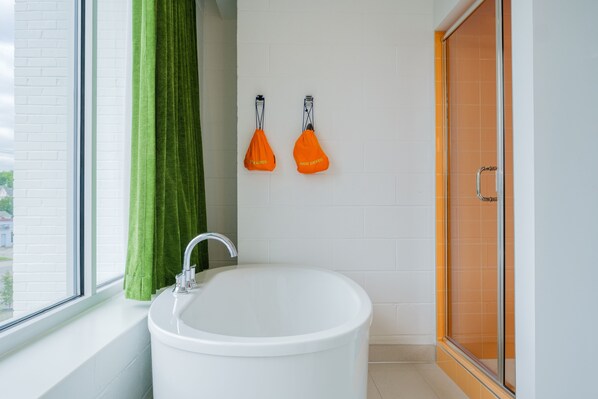 A bathroom with a white bathtub, a green shower curtain, and two orange hair dryers hanging on the wall.