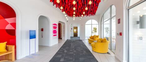 Un vestíbulo de hotel con un pasillo central alfombrado, decoración colgante roja y un sofá amarillo.