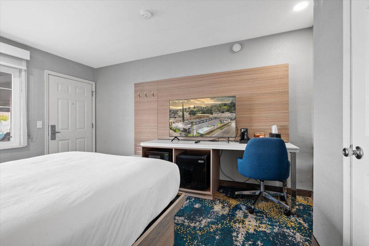 Habitación de hotel con cama, escritorio con computadora, silla y ventana grande.