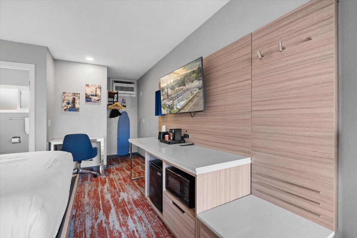 Quarto de hotel moderno com uma cama, uma escrivaninha com cadeira, micro-ondas, um frigorífico pequeno e televisão na parede.