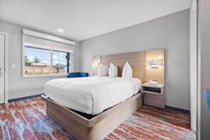 Un dormitorio moderno con una cama grande, una mesita de noche, una lámpara de pared y una ventana con vistas al exterior.