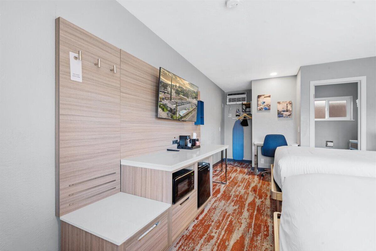 A compact hotel room with a kitchenette, a bed, a desk, and a chair.