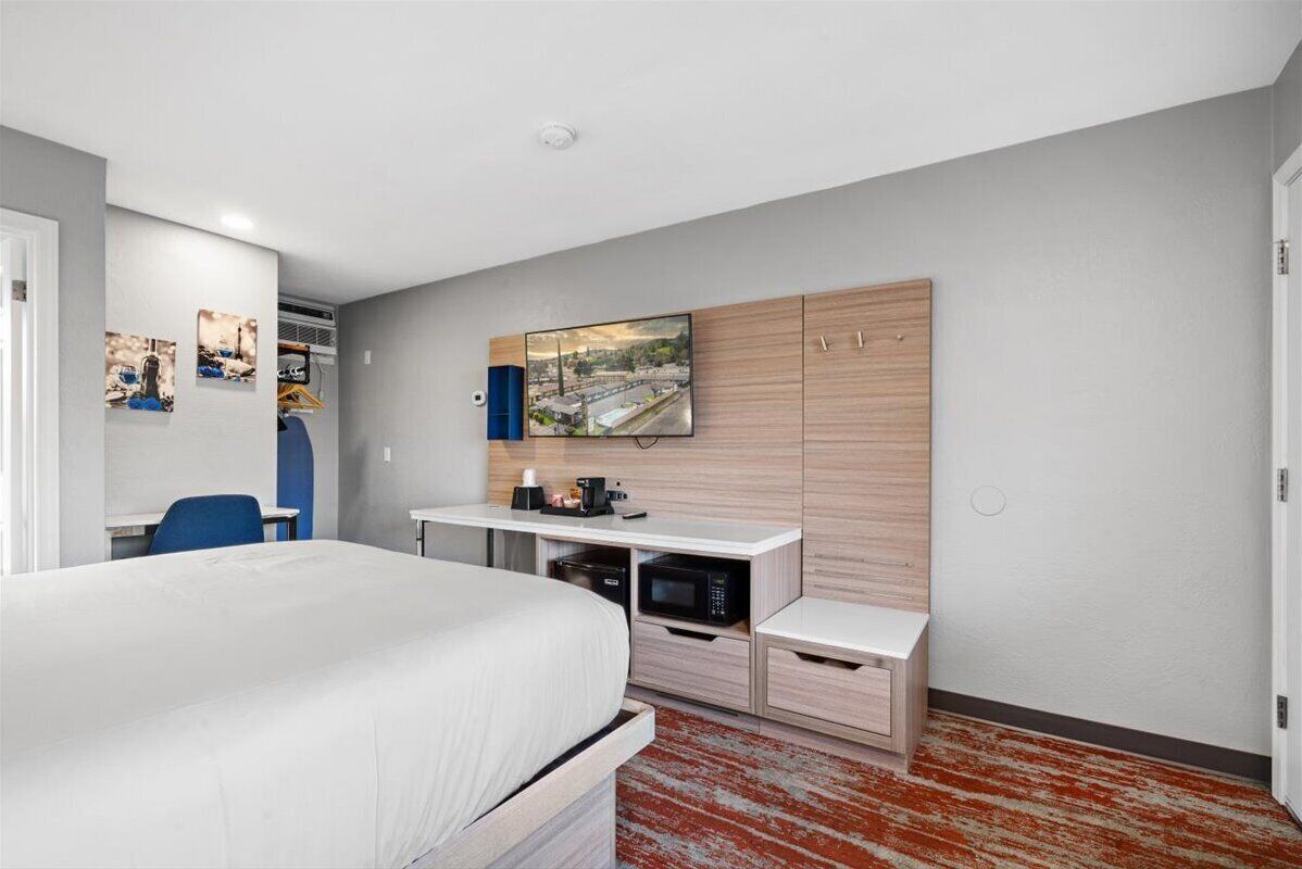 Una habitación de hotel moderna con una cama, un escritorio, un televisor de pantalla plana y un microondas.
