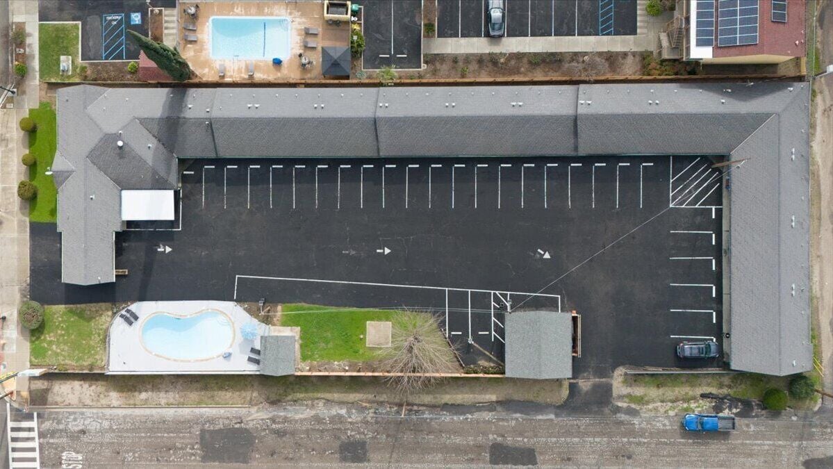 Vista aérea de um edifício com estacionamento, piscina e um pequeno jardim.