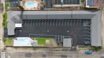 Vista aérea de um edifício com estacionamento, piscina e um pequeno jardim.