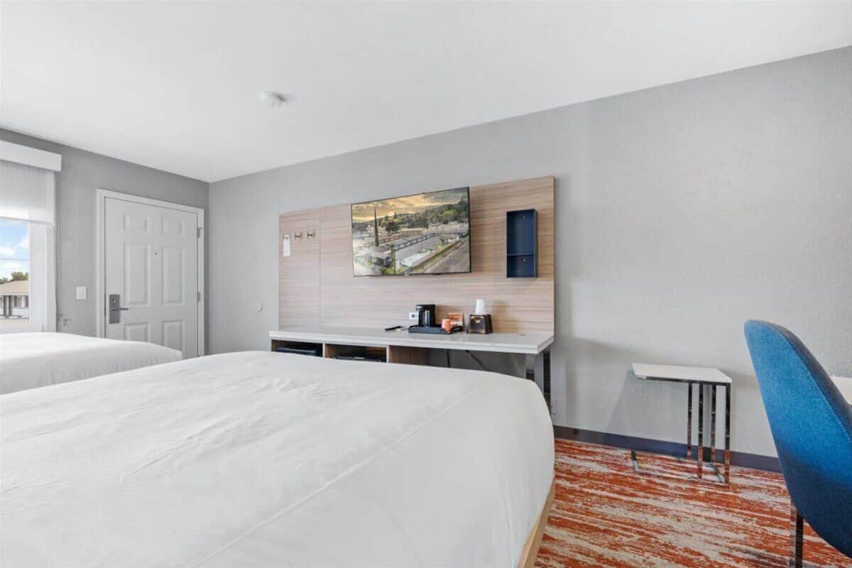 A hotel room with two beds, a desk with a coffee maker, a chair, and a large cityscape painting on the wall.
