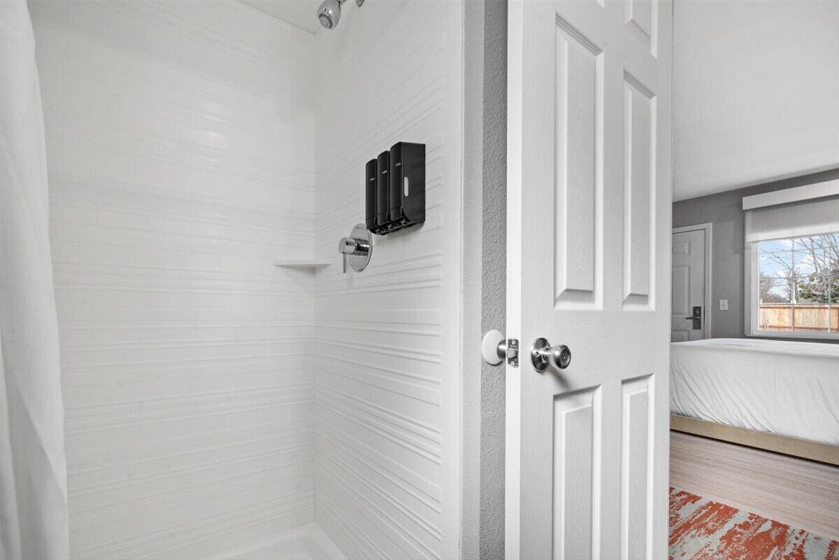 Un baño moderno con ducha, inodoro y lavamanos. Hay una puerta que conduce a otra habitación.