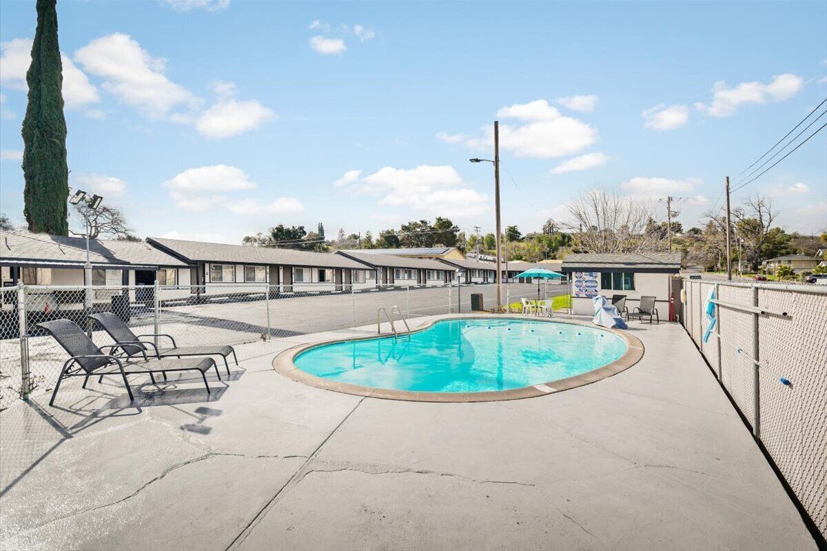 A motel with a swimming pool, lounge chairs, and a fenced area.