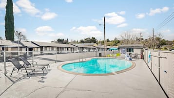 A motel with a swimming pool, lounge chairs, and a fenced area.