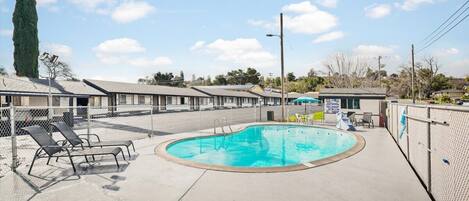 A motel with a swimming pool, lounge chairs, and a fenced area.