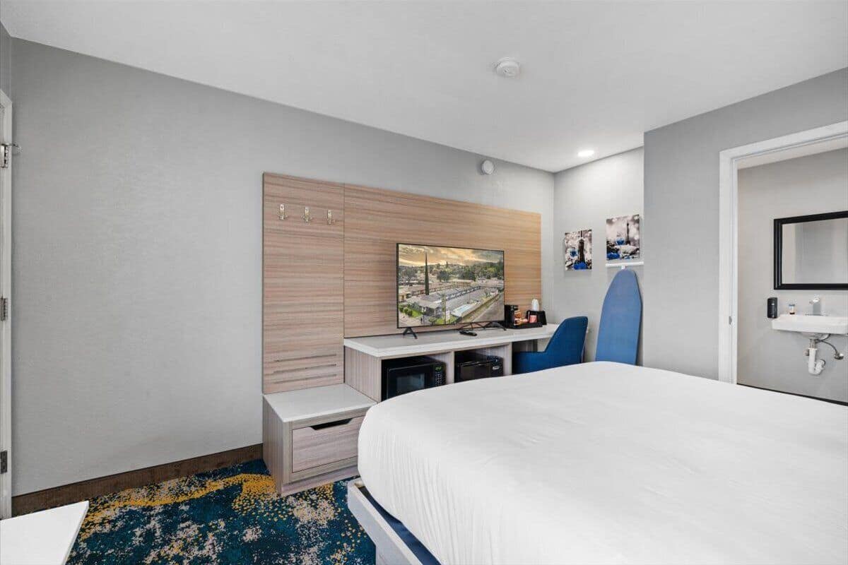 A hotel room with a bed, a desk with a computer, a television, and a small bathroom.