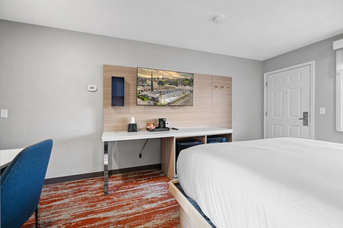 Une chambre d’hôtel comprenant un lit, un bureau avec une chaise, un téléviseur à écran plat fixé au mur et une vue sur le paysage urbain.