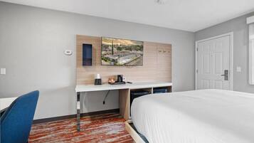 Une chambre d’hôtel comprenant un lit, un bureau avec une chaise, un téléviseur à écran plat fixé au mur et une vue sur le paysage urbain.