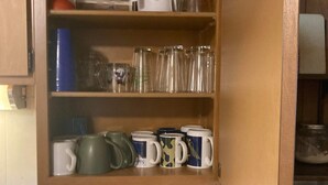 A kitchen with wooden cabinets, a coffee maker, and various mugs and glassware on the shelves. - Beautiful cabin on the Manistee River (Mesick)