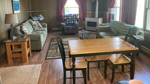 A cozy living room with a fireplace, a wooden table, and comfortable seating. - Beautiful cabin on the Manistee River (Mesick)
