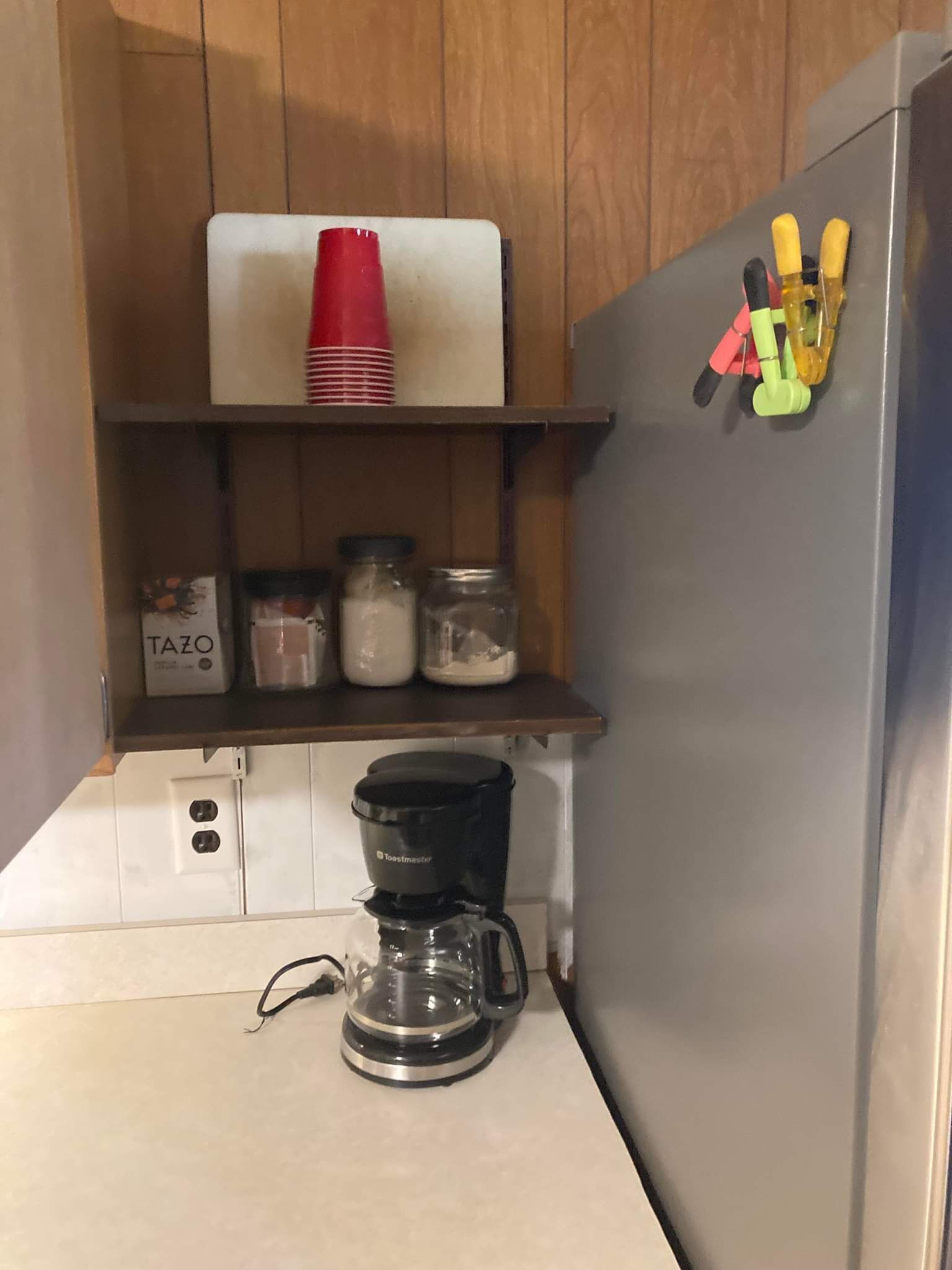 Eine Küche mit einem Toaster, einer Kaffeemaschine und Regalen voller Gläser und einer roten Tasse.