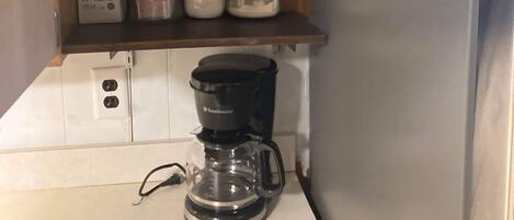 Eine Küche mit einem Toaster, einer Kaffeemaschine und Regalen voller Gläser und einer roten Tasse.