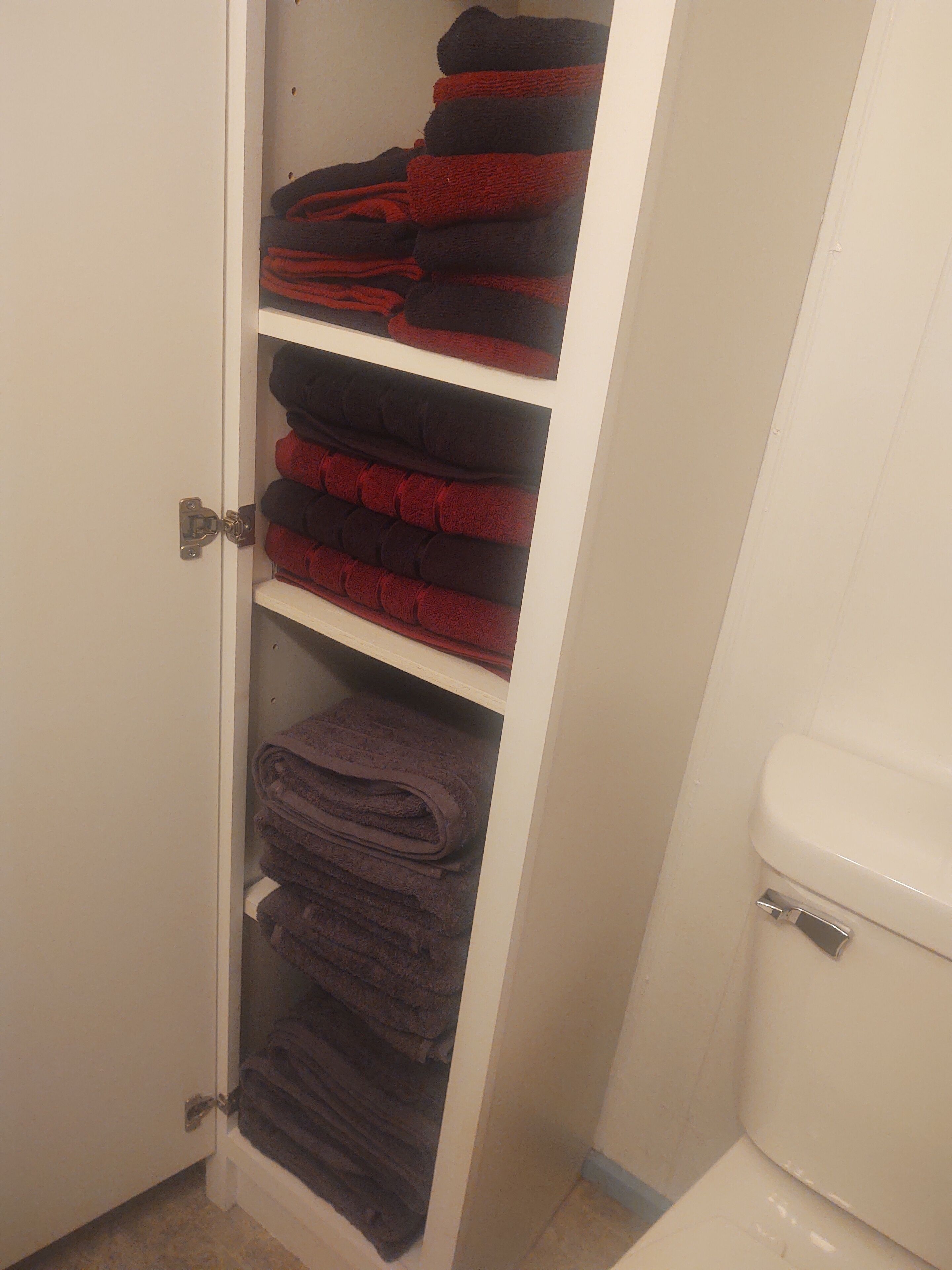 A bathroom with a toilet and a storage cabinet with towels.
