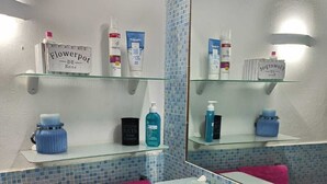 Une salle de bain avec un lavabo blanc, des serviettes roses et divers produits de toilette rangés sur des étagères.