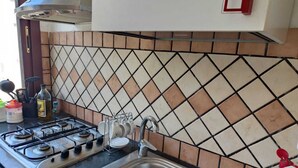 Une cuisine équipée d’une cuisinière à gaz, d’un évier et d’un plan de travail carrelé.