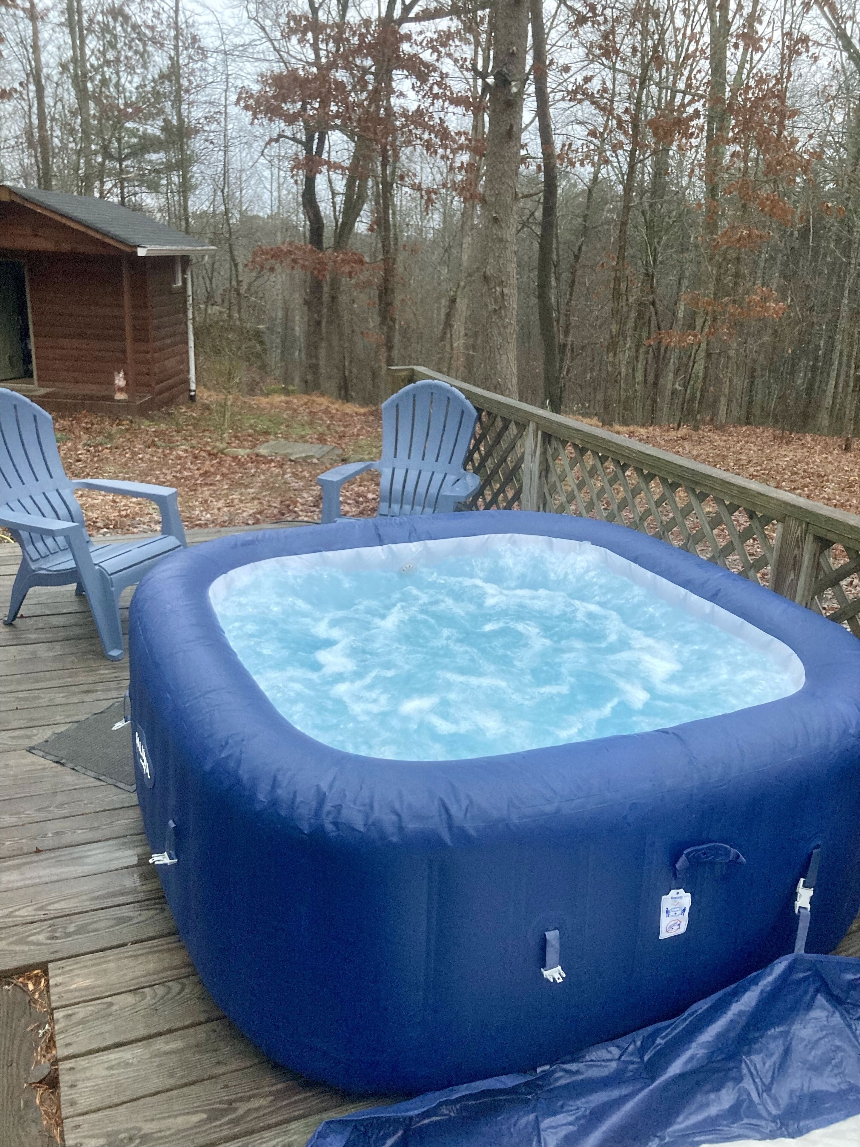 Un jacuzzi en una terraza de madera, con dos sillas Adirondack y una cabaña de madera al fondo.