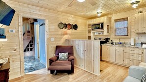 Un intérieur en bois avec un ventilateur de plafond, une cuisine équipée d’un four à micro-ondes et un coin salon avec un fauteuil marron.