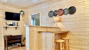 Un intérieur en bois avec un coin bar, des tabourets, un téléviseur à écran plat et des assiettes décoratives accrochées au mur.