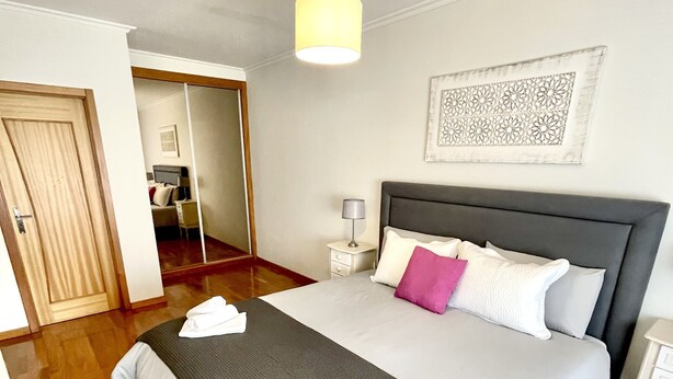 Ein ordentlich eingerichtetes Schlafzimmer mit einem großen Bett, einem Nachttisch mit Lampe und einem Spiegel.