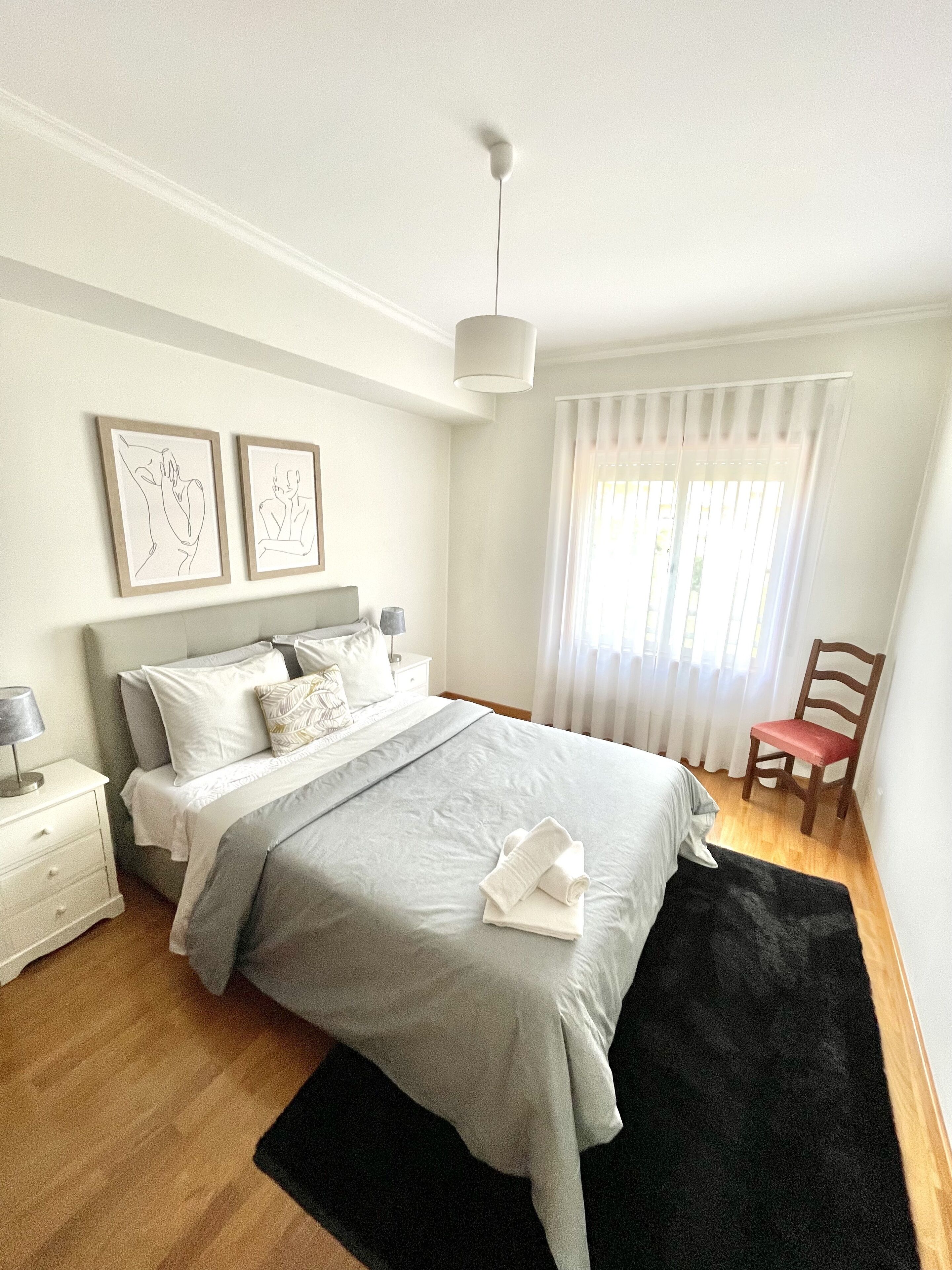 A modern bedroom with a bed, bedside tables, a chair, and artwork on the wall.