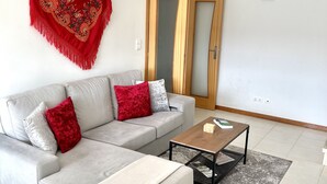 Ein Wohnzimmer mit grauem Sofa, roten und silbernen Kissen, einem Holztisch und einem grauen Teppich mit Muster.