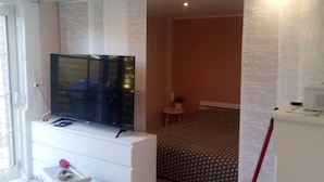 Un dormitorio con una cama, un televisor sobre un mueble, una mesita y una silla.