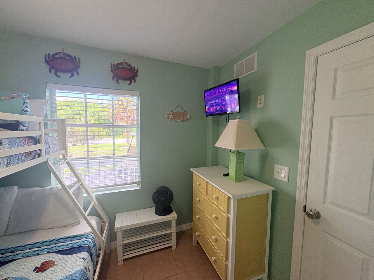 A room with bunk beds, a television, a dresser, and a window with blinds.