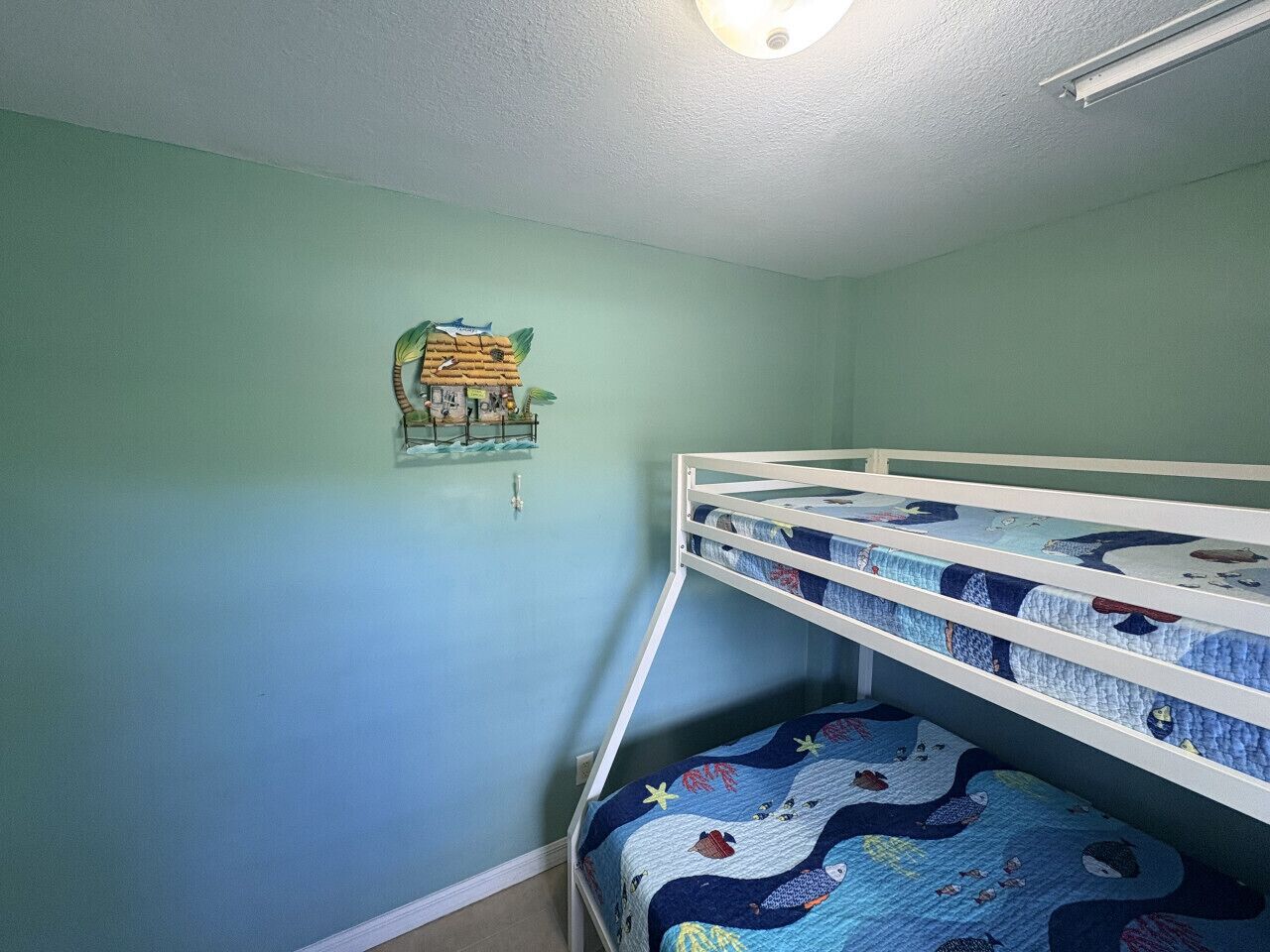 A bunk bed room with a green wall and a decorative piece above the bed.