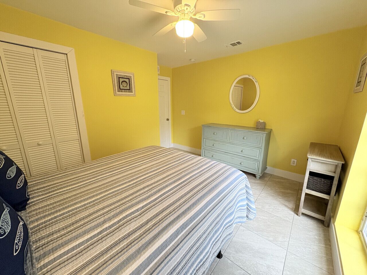 A bedroom with a bed, a dresser, a vanity, and a ceiling fan.