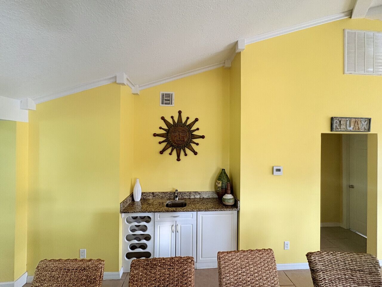 A compact living space with a kitchen area, a dining table with four chairs, and a sun-shaped wall decoration.