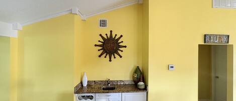 A compact living space with a kitchen area, a dining table with four chairs, and a sun-shaped wall decoration.