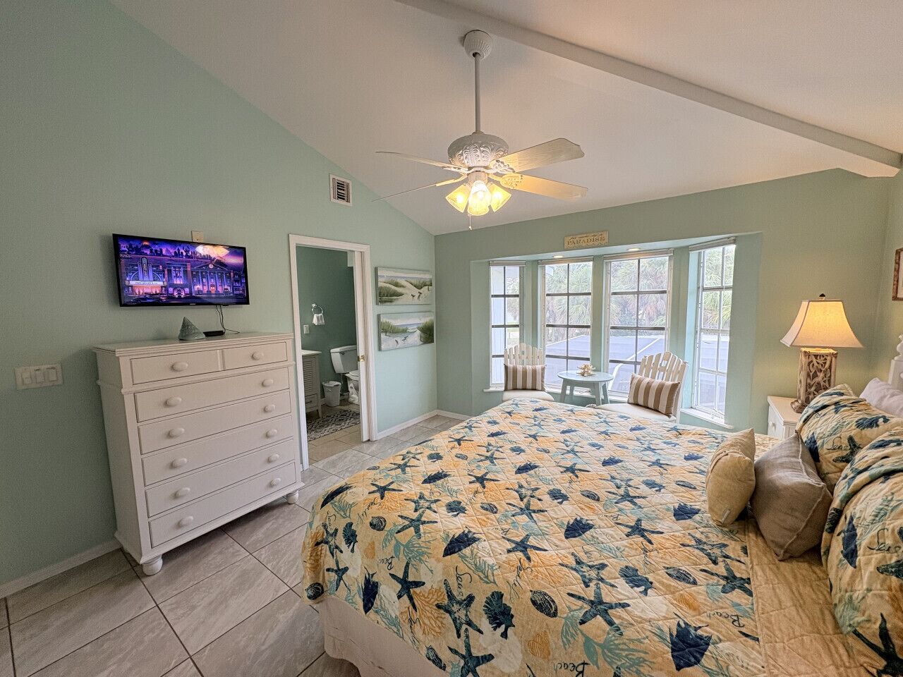Une chambre à coucher comprenant un lit, une commode, un téléviseur et un ventilateur de plafond.