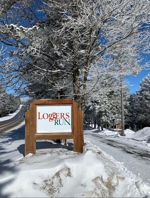 Ein hölzernes Schild mit dem Schriftzug 'Loggers Run' in einer verschneiten, ländlichen Umgebung.