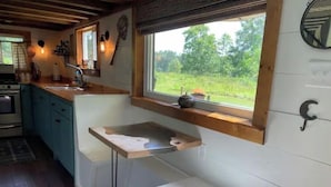 Uma cozinha compacta com bancada de madeira, pia embutida e janela com vista para uma paisagem verde.