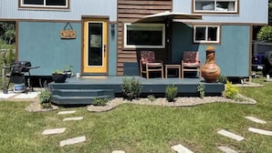 Uma casa móvel com varanda, duas cadeiras, uma mesa e um vaso grande.