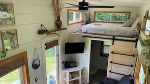 Quarto estilo loft compacto com cama, televisão e um pequeno espaço para sentar.