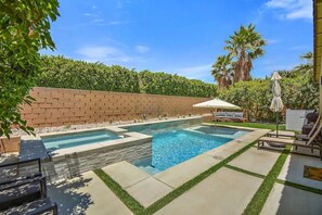 Relax by the pool surrounded by lush greenery and a brick wall.