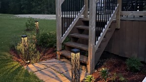 Una escalera de madera conduce a una terraza con barandillas, rodeada por un jardín ajardinado con plantas pequeñas y un sendero de piedra.