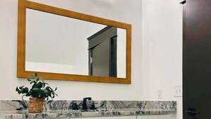 A bathroom with a marble countertop, a wooden-framed mirror, and a potted plant.